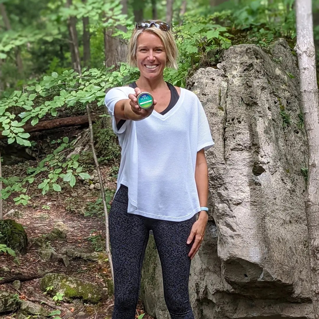 Smiling woman holding out a No Pong tin in a forest