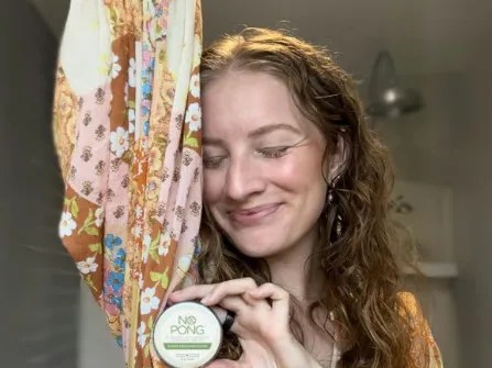 A No Pong customer with long curly hair, eyes closed and smiling, holding up her tin with one arm raised