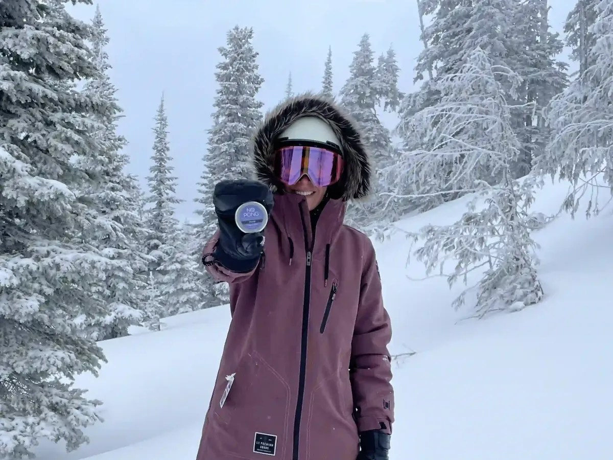 A No Pong customer in a ski jacket and goggles holding up her tin in the snow