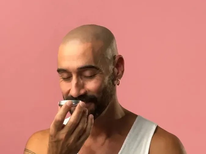 A No Pong customer on a pink background, eyes closed, smelling his open tin